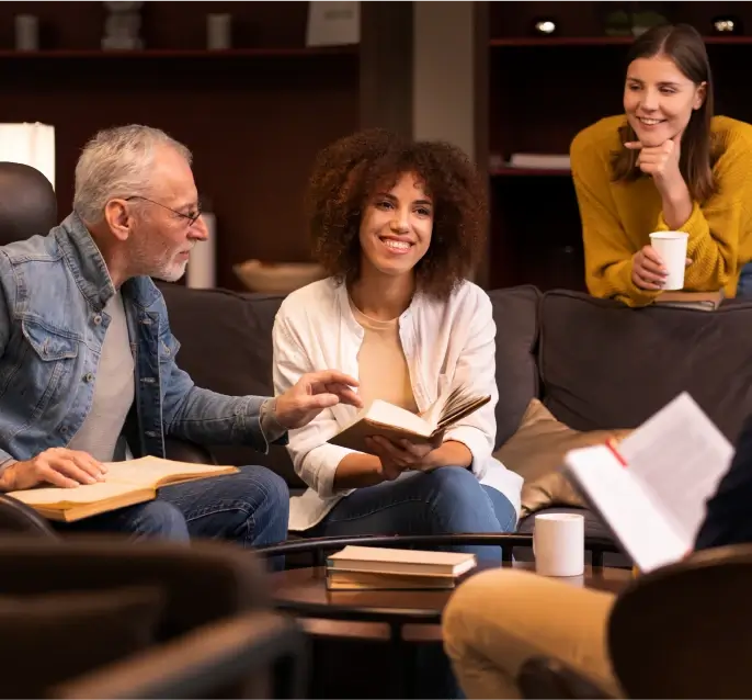 A diverse group of adults sitting on a sofa and chatting with books in hand, enjoying a relaxed book club meeting.