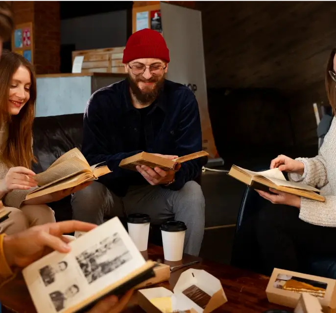 Friends gathered in a casual cafe setting, reading books and smiling while enjoying coffee and desserts.